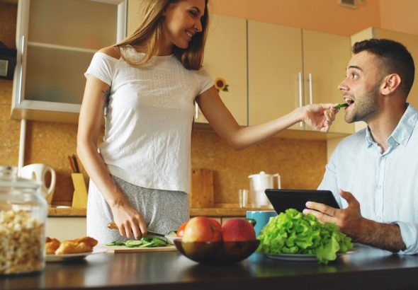 Attractive couple chatting in the kitchen early morning. Beautiful woman feed her husband while cooking breakfast at home
