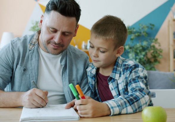 Caring father creative man is drawing pictures while kid is watching sitting at desk in house enjoying time together. Family activities and lifestyle concept.